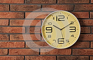 Stylish analog clock hanging on brick wall.