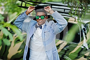 Stylish arabian man at sunglasses, cap and bow tie posed against military car. Arab model boy