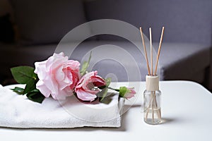 Stylish aromatic reed diffuser with pink roses flowers on the white table in the grey bedroom at night