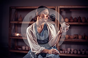 Stylish artisan girl works with clay on a potter& x27;s wheel. Craft manufacture.