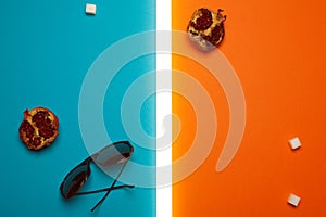 Stylish and arty eyewear concept in avant-garde style. Trendy sunglasses on blue and orange background with pomegranates, sugar