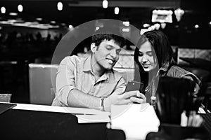 Stylish asian couple wear on jeans sitting on chair at bar in club and look on phone