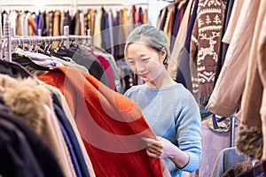 Stylish Asian woman is choosing second hand sweater from the clothing shop for winter season fashion to keep warm at the new year