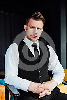 Stylish athletic man in a business costume vest. Sits in the director`s chair, a serious look.