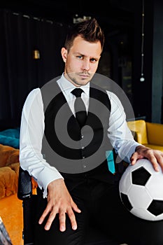 Stylish athletic man in a business suit and a soccer ball. Against the background of a loft wall.