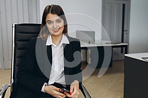 Stylish attractive young businesswoman with a lovely smile sitting in front of a table in the office grinning at the camera