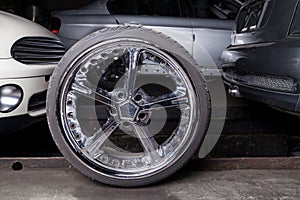 Stylish auto wheel with shiny chrome tuned disc in a repair shop between cars background for tire station or banner