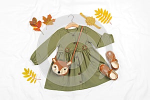 Stylish autumn set of child clothes. Green dress, brown bag, shoes, accessories for hair and autumn leaves on white background.