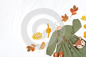 Stylish autumn set of child clothes. Green dress, brown bag, shoes and yellow tights, accessories for hair and autumn leaves on