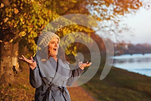 Stylish autumn woman throwing fallen leaves in park. Autumn fashion, lifestyle concept. Happy girl enjoying sunny autumn weather