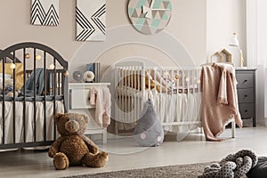 Stylish baby bedroom for twins with two cribs and teddy bear on the floor