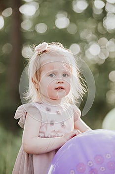 Stylish baby girl 2-5 year old holding big balloon wearing trendy pink dress in meadow. Playful