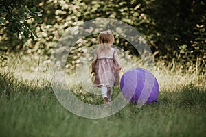 Stylish baby girl 2-5 year old holding big balloon wearing trendy pink dress in meadow. Playful