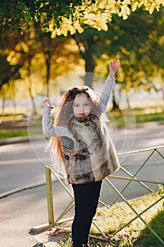 Stylish baby girl 4-5 year old wearing boots, fur coat standing in park. Looking at camera. Autumn fall season