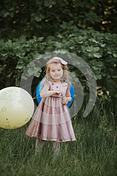 Stylish baby girl holding big balloon wearing trendy pink dress in meadow. Playful. Birthday party