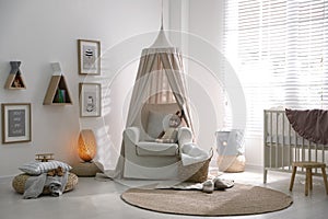 Stylish baby room interior with crib and comfortable armchair