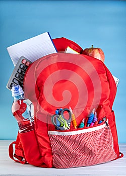 Stylish backpack with various school stationary on a white wooden table on a blue background