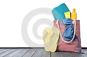 Stylish bag with beach accessories on grey wooden table against white background