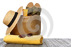 Stylish bag with beach accessories on grey wooden table against white background