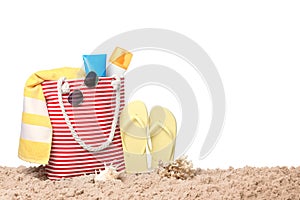 Stylish bag with beach accessories on sand against white background