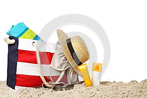 Stylish bag with beach accessories on sand against white background