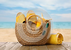 Stylish bag with beach accessories on wooden surface near seashore