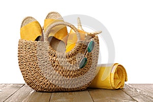 Stylish bag with beach accessories on wooden table against white background