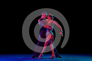 Stylish ballroom dancers couple in gorgeous outfits dancing in sensual pose on dark background in neon light. Concept of