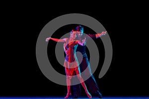 Stylish ballroom dancers couple in gorgeous outfits dancing in sensual pose on dark background in neon light. Concept of