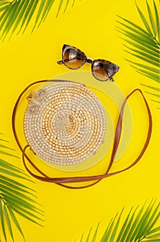 Stylish bamboo bag framed with palm leaves. Minimal summer concept on a yellow sun background