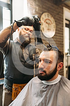 Stylish barber drying mans hair in barbershop