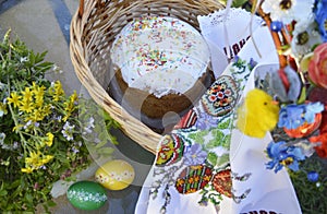 Stylish basket with painted eggs, bread with spring flowers at sunny day, top view.