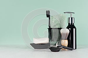 Stylish bathroom interior with black shaving accessories on green  wall, white table - razor, toothbrush, towel, soap, shave brush photo