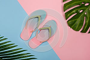 Stylish beach flip-flops on pink and blue pastel background with monstera and plam leaves Summer concept with copy space