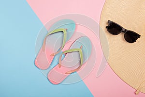 Stylish beach flip-flops, sunglasses and sun hat on pink and blue pastel background, top view. Summer concept with copy