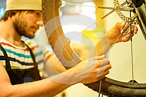 Stylish bearded bicycle mechanic doing his professional work in workshop - Young trendy man checking spoke wheel - Repairing bikes