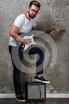 Stylish bearded guy with guitar against concrete wall