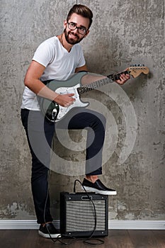 Stylish bearded guy with guitar against concrete wall