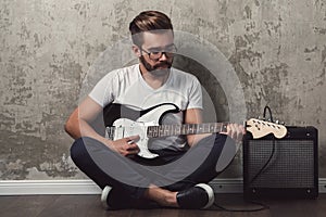 Stylish bearded guy with guitar against concrete wall