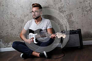 Stylish bearded guy with guitar against concrete wall