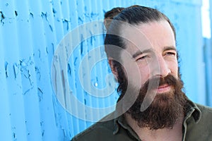 Stylish bearded hipster model with man bun hairstyle, lifestyle in the street, depth of field. Blue background