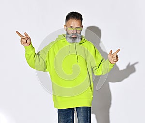 Stylish bearded middle aged man hipster in yellow hoodie and glasses dances with fingers up, points different directions