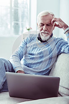 Stylish bearded retired man wearing blue sweater using his silver laptop