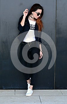 Stylish beautiful ginger young woman standing by the wall on the street. Streetstyle photo shoot.