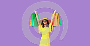 Stylish beautiful happy young woman with shopping bags in summer straw hat on purple background