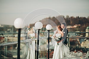 Stylish beautiful wedding couple kissing and hugging on background panoramic view of the old town