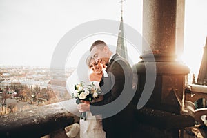 Stylish beautiful wedding couple kissing and hugging on background panoramic view of the old town