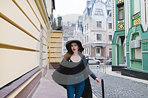 A stylish beautiful woman poses to the camera on the backdrop of a beautiful old town street.