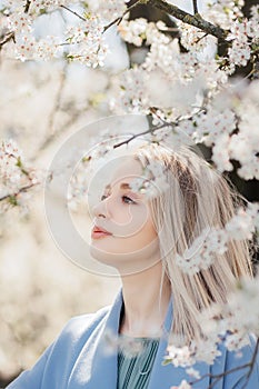 Stylish beautiful woman sensually posing among blooming apple branches in sunny spring, calm moment. Portrait of happy young