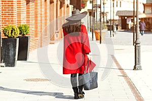 Stylish beautiful woman walking in street. Girl wearing red coat, black hat and holding trendy bag. Fashion outfit, autumn trend,